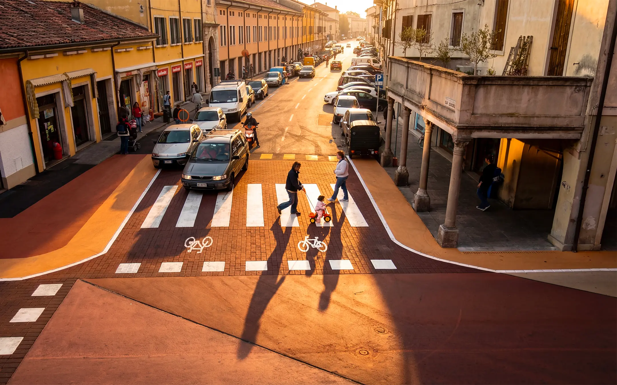 Incrocio urbano al tramonto con attraversamento ciclopedonale in asfalto stampato e colorato